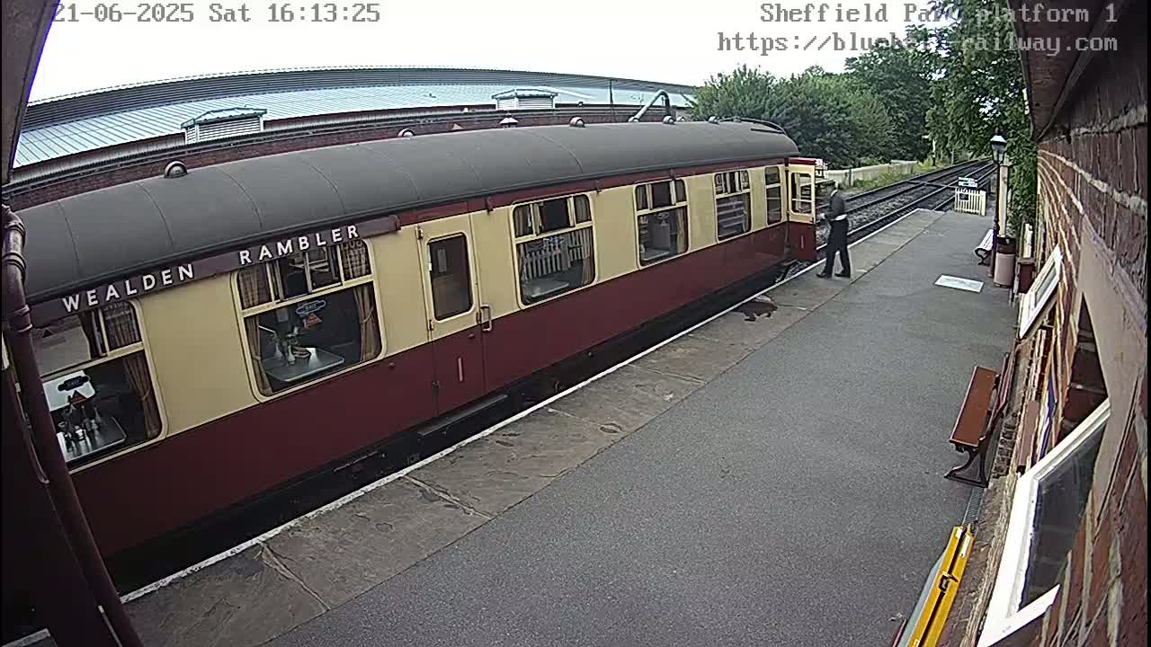 A maroon and cream passenger train car is stopped at a train platform on an overcast day.