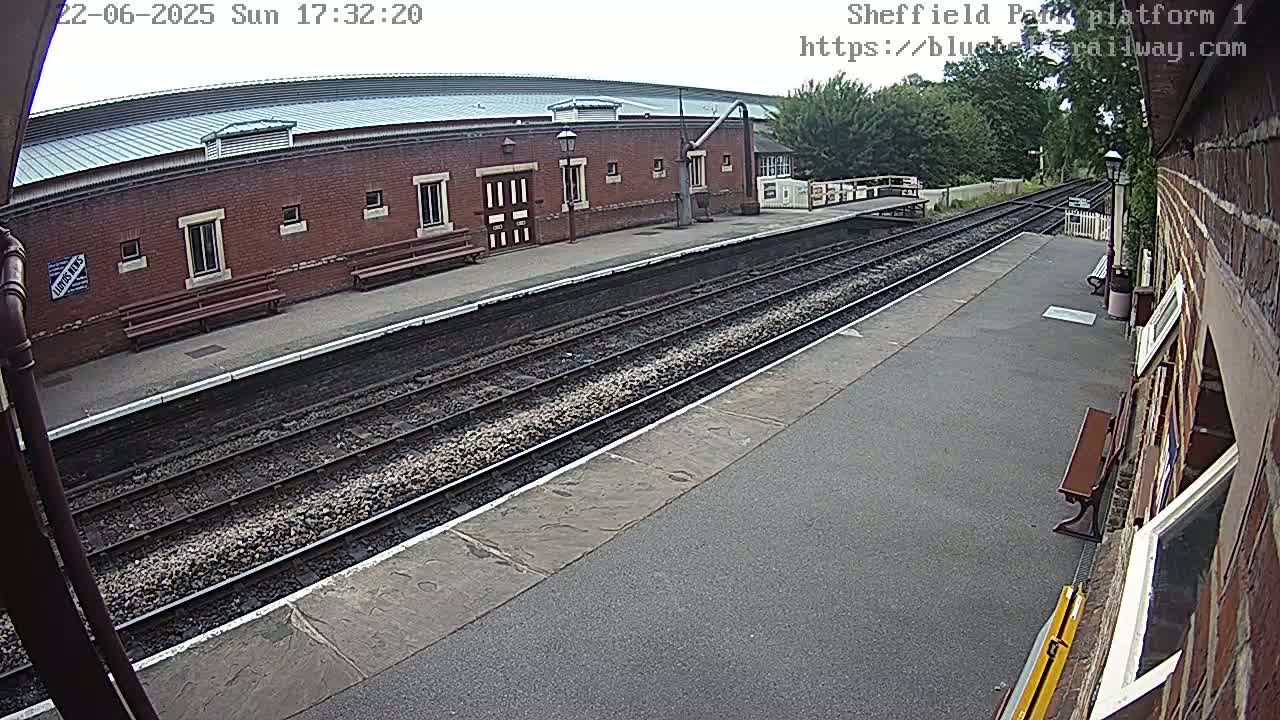A mostly sunny view of a train platform with two train tracks and a brick building.