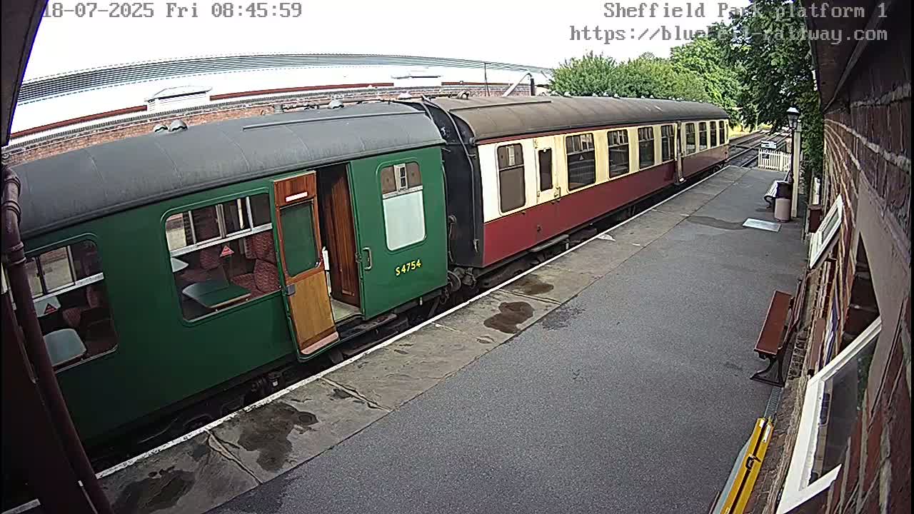 A green and maroon passenger train is at a station platform on an overcast day.
