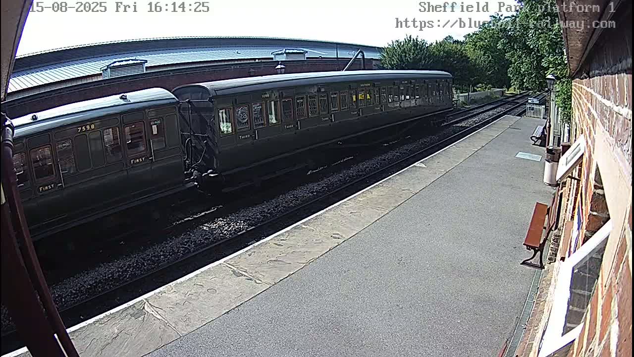 A green and maroon passenger train is at a station platform on an overcast day.