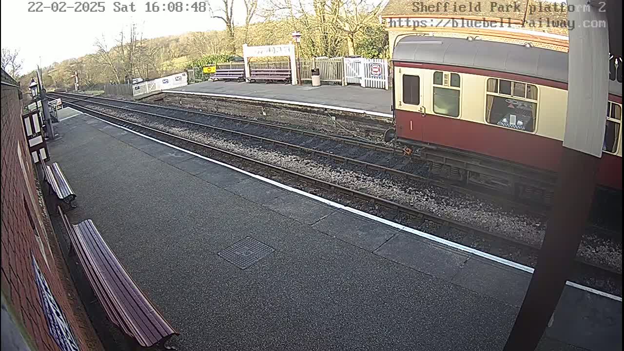 A red and cream train is parked at a railway station platform on a partly sunny day.