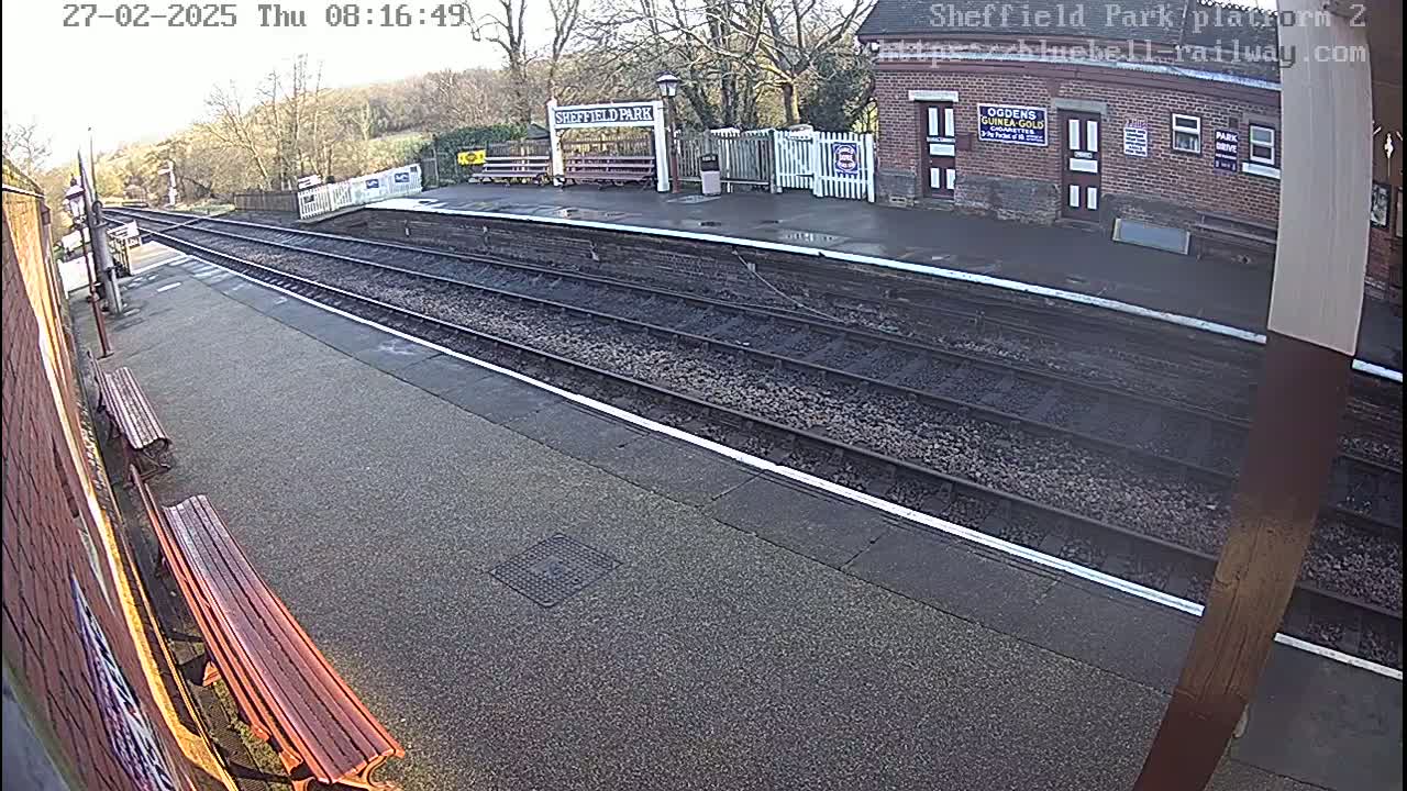 A train platform with two benches and train tracks is shown on an overcast day.