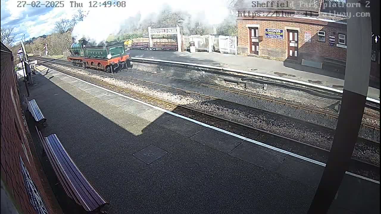 A steam train departs a railway station on a sunny day.