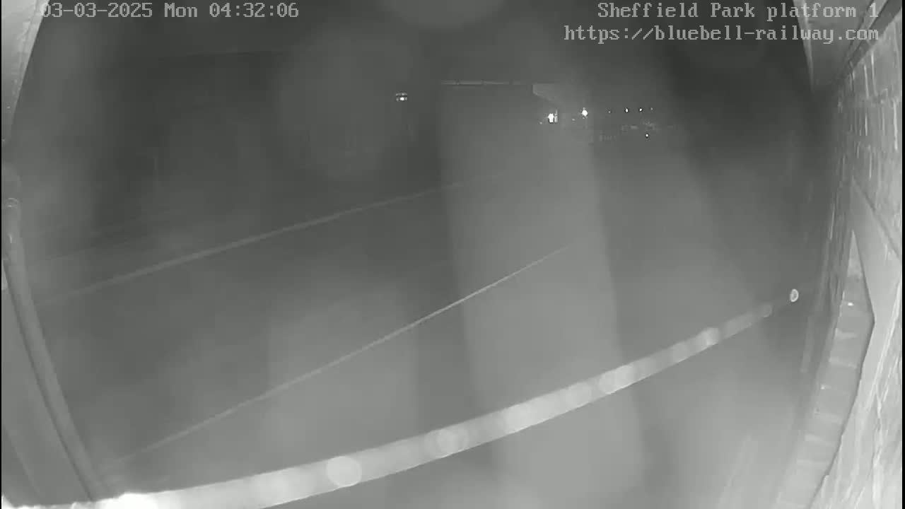 A nighttime, low-light security camera view shows an empty platform area with faint lines on the ground.