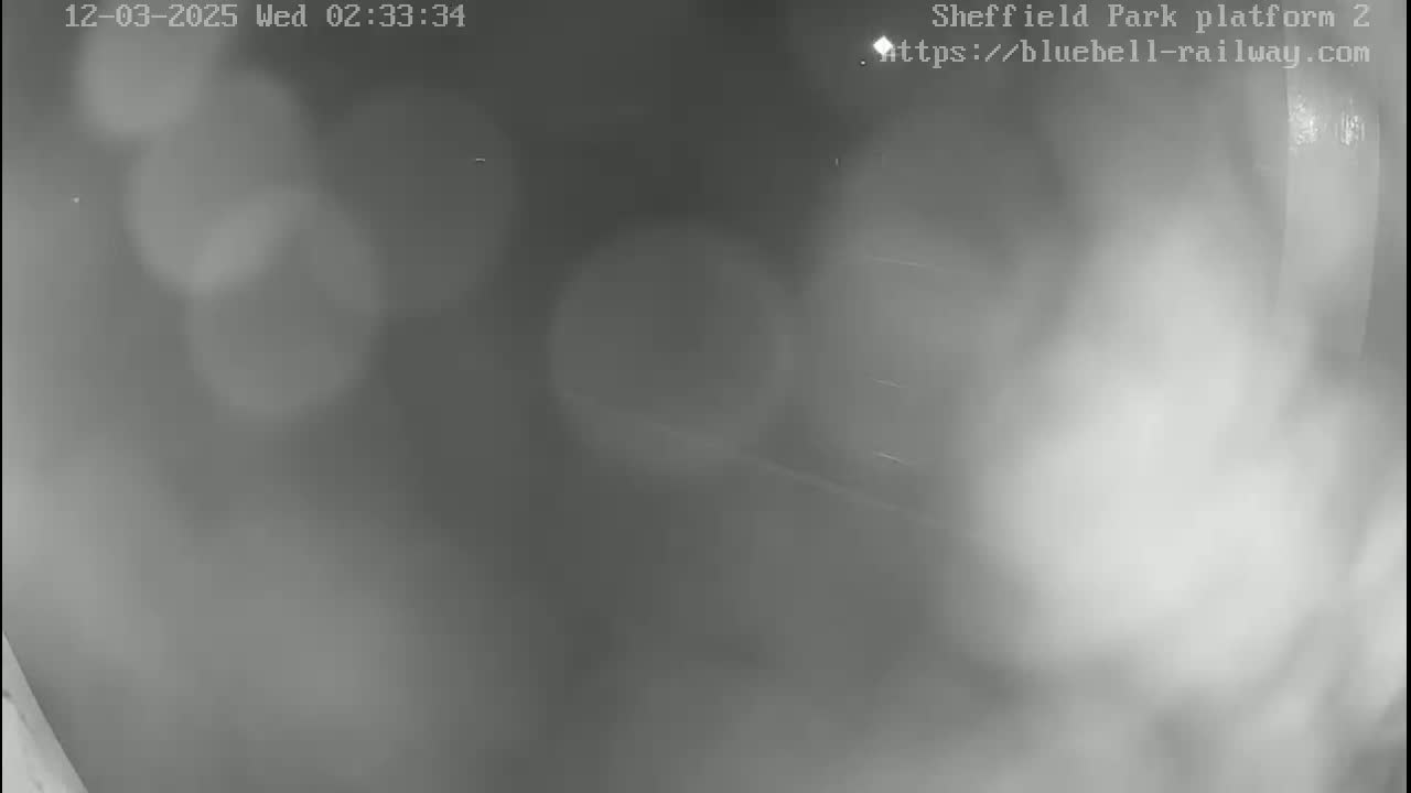 A blurry, nighttime image shows an indistinct outdoor scene with what appears to be light rain or fog.