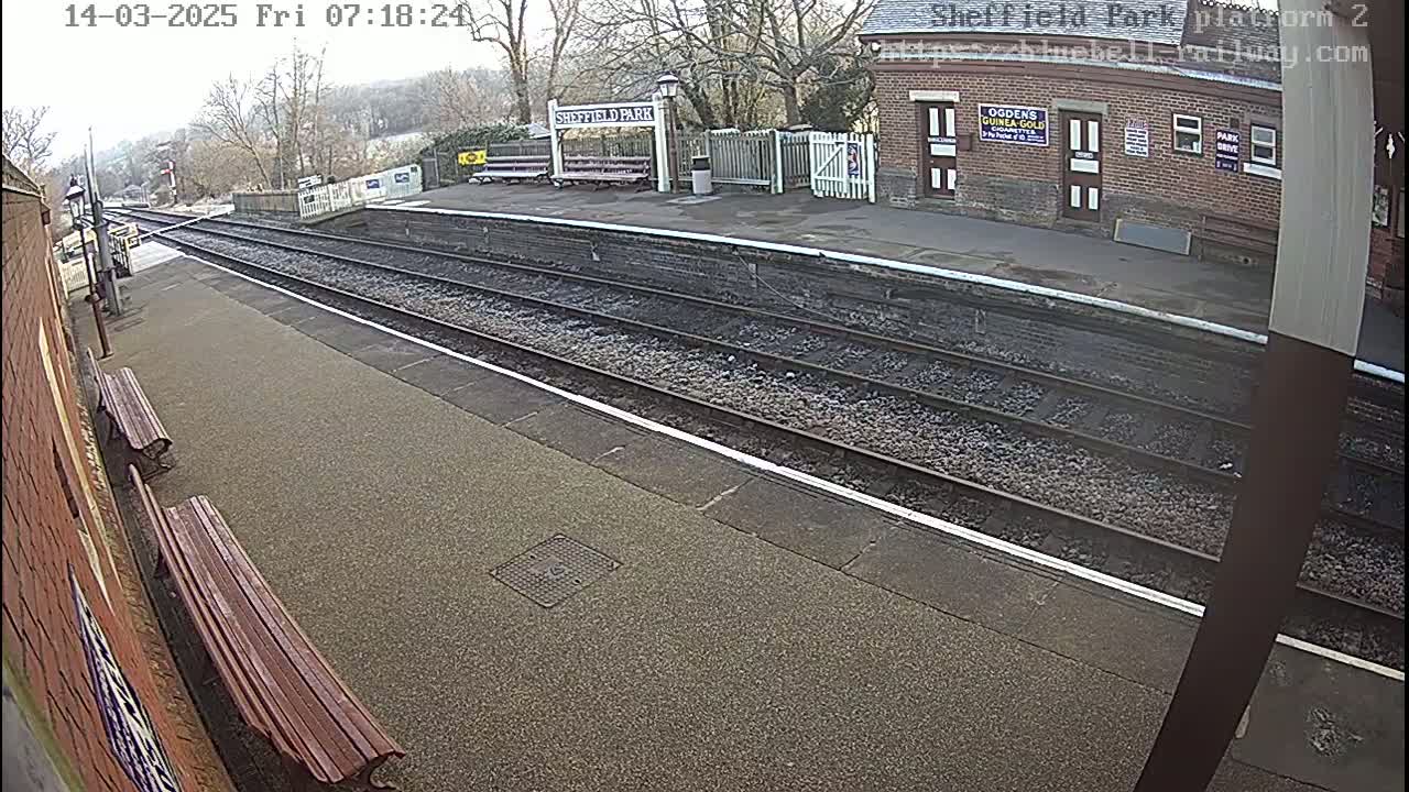 A mostly empty train platform on an overcast day with two wooden benches and train tracks extending into the distance.