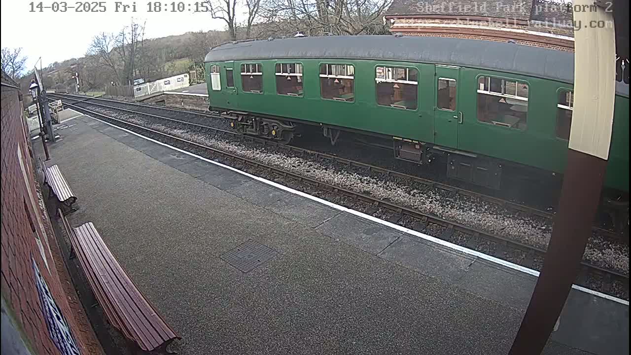 A green railway carriage is stopped at a station on a mostly cloudy day.
