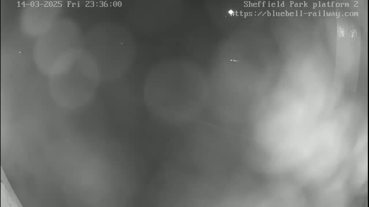 A blurry, low-light nighttime image shows a mostly empty platform with some faint light sources visible in the distance.