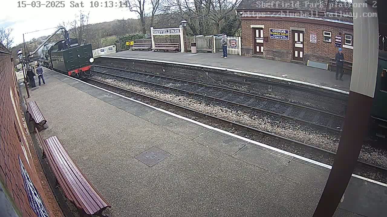 A steam train arrives at a train station platform on a sunny day.