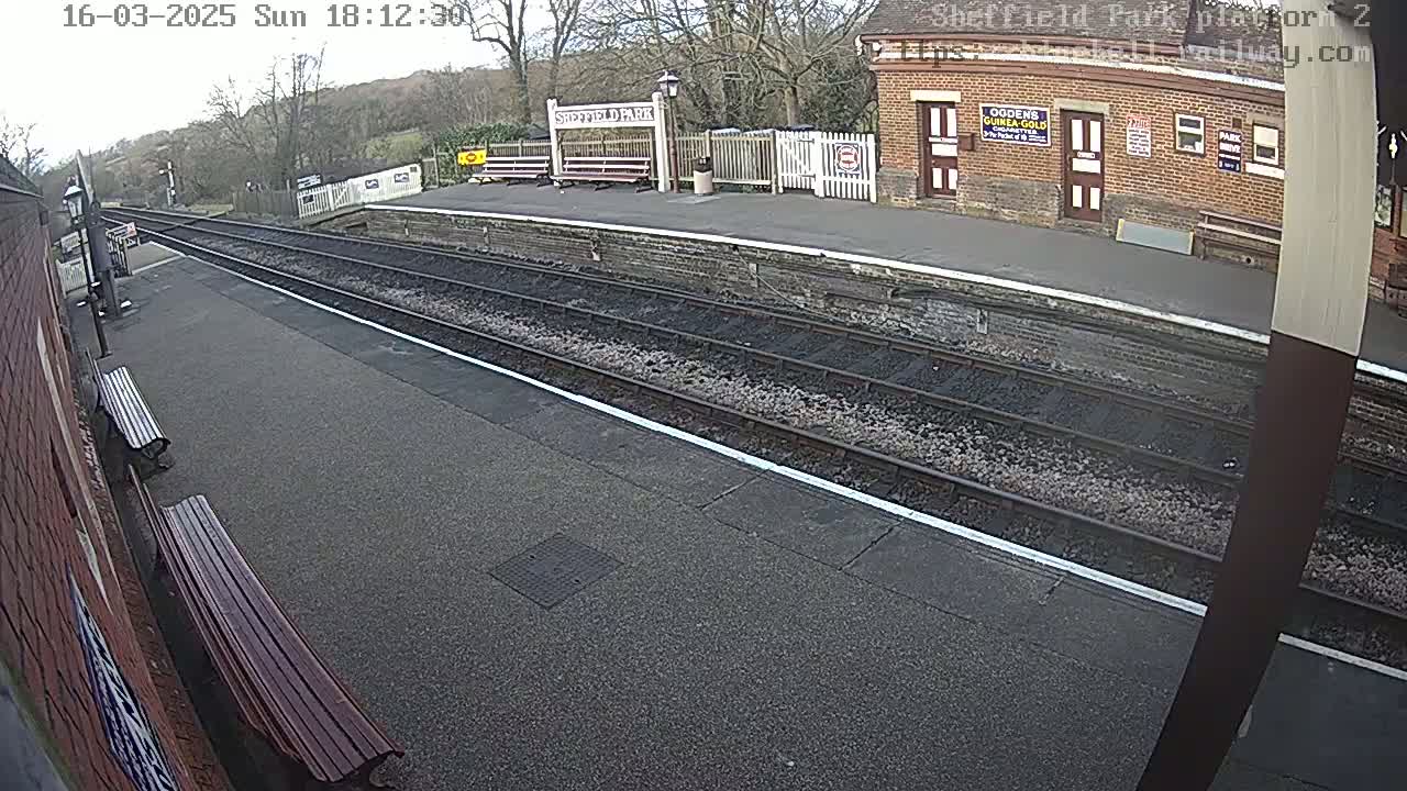 A train platform with empty benches and train tracks under an overcast sky.