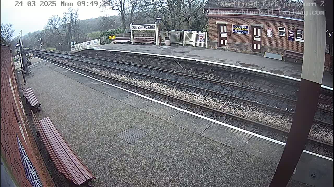 A mostly cloudy day at a train station platform with two benches and multiple train tracks.