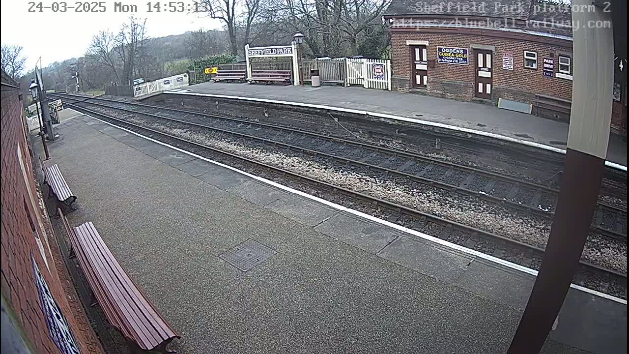 A train platform with two empty benches and train tracks under an overcast sky.