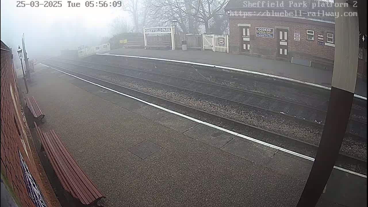 A foggy view of a train platform with two benches and train tracks extending into the distance.