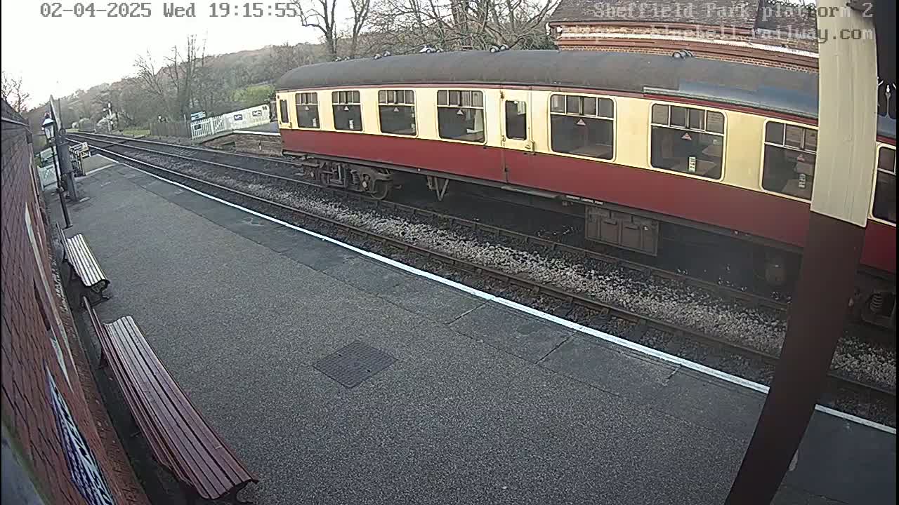 A red and cream railway carriage sits at a station on a cloudy day.