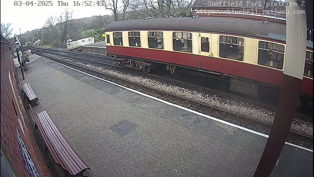 A red and cream railway carriage is parked at a station platform on an overcast day.