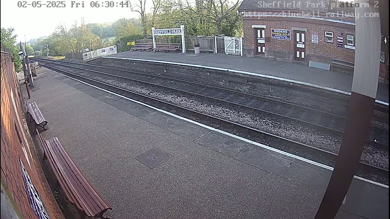 A mostly overcast view of an empty train platform with two benches and train tracks extending into the distance.