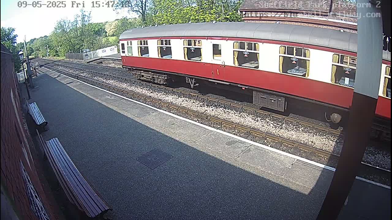 A red and white passenger train is parked at a sunny train station platform.