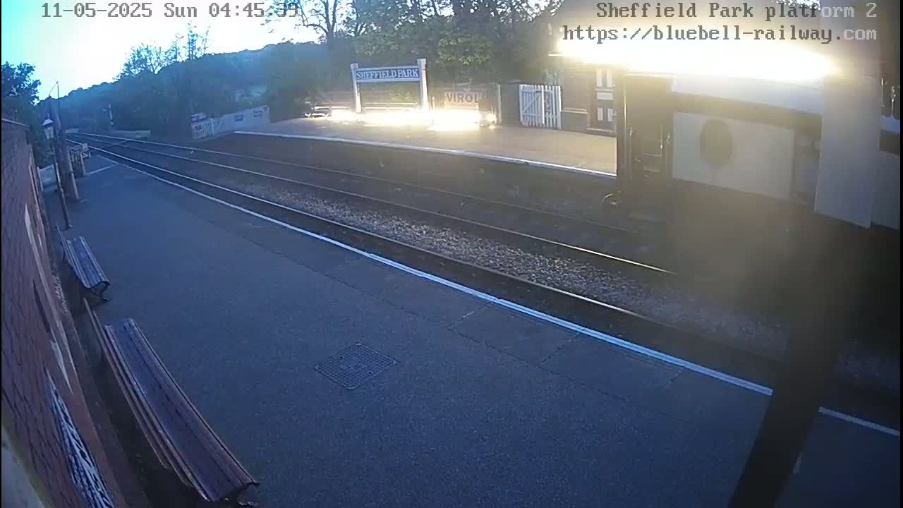 A dimly lit train platform at dawn, with two empty benches and train tracks extending into the background.