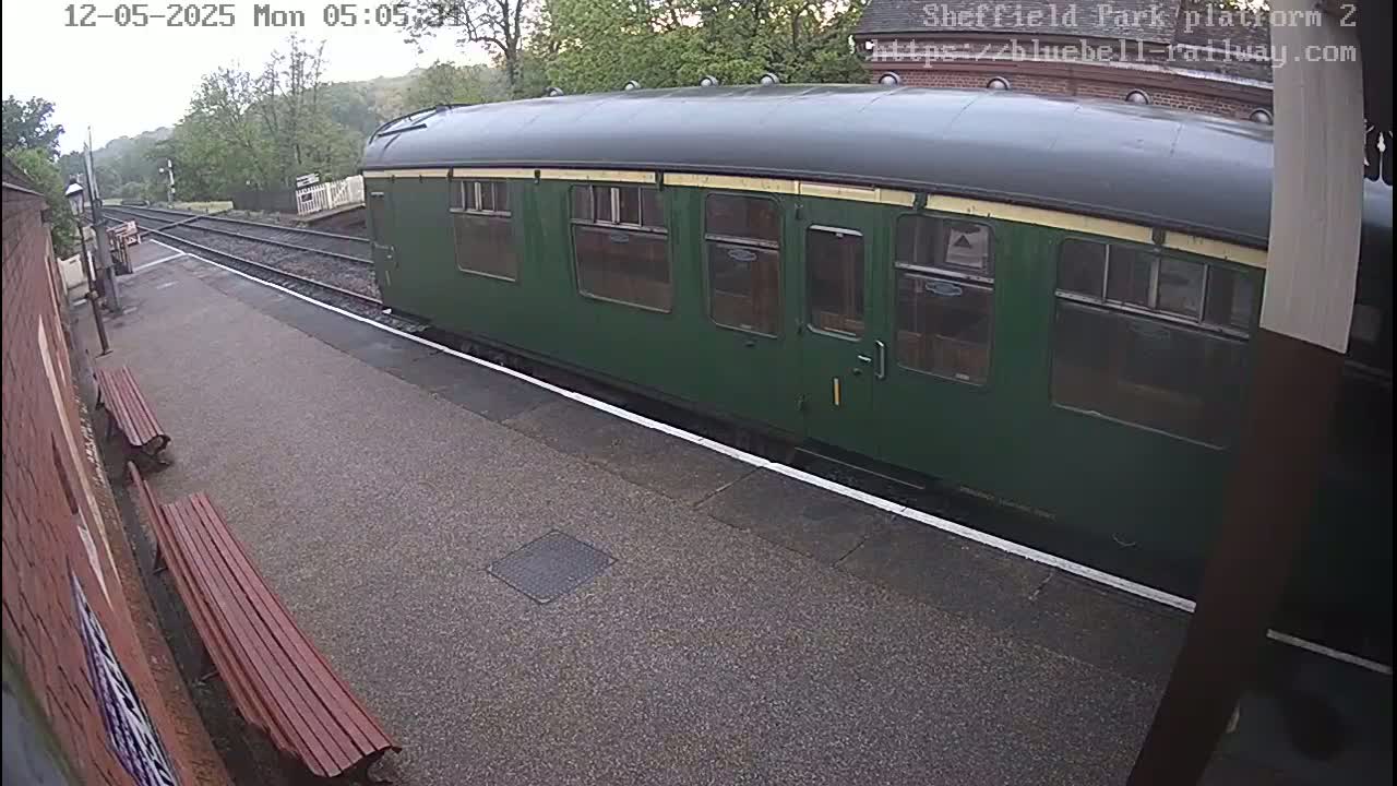 A dark green passenger train car is stopped at a station platform on an overcast day.