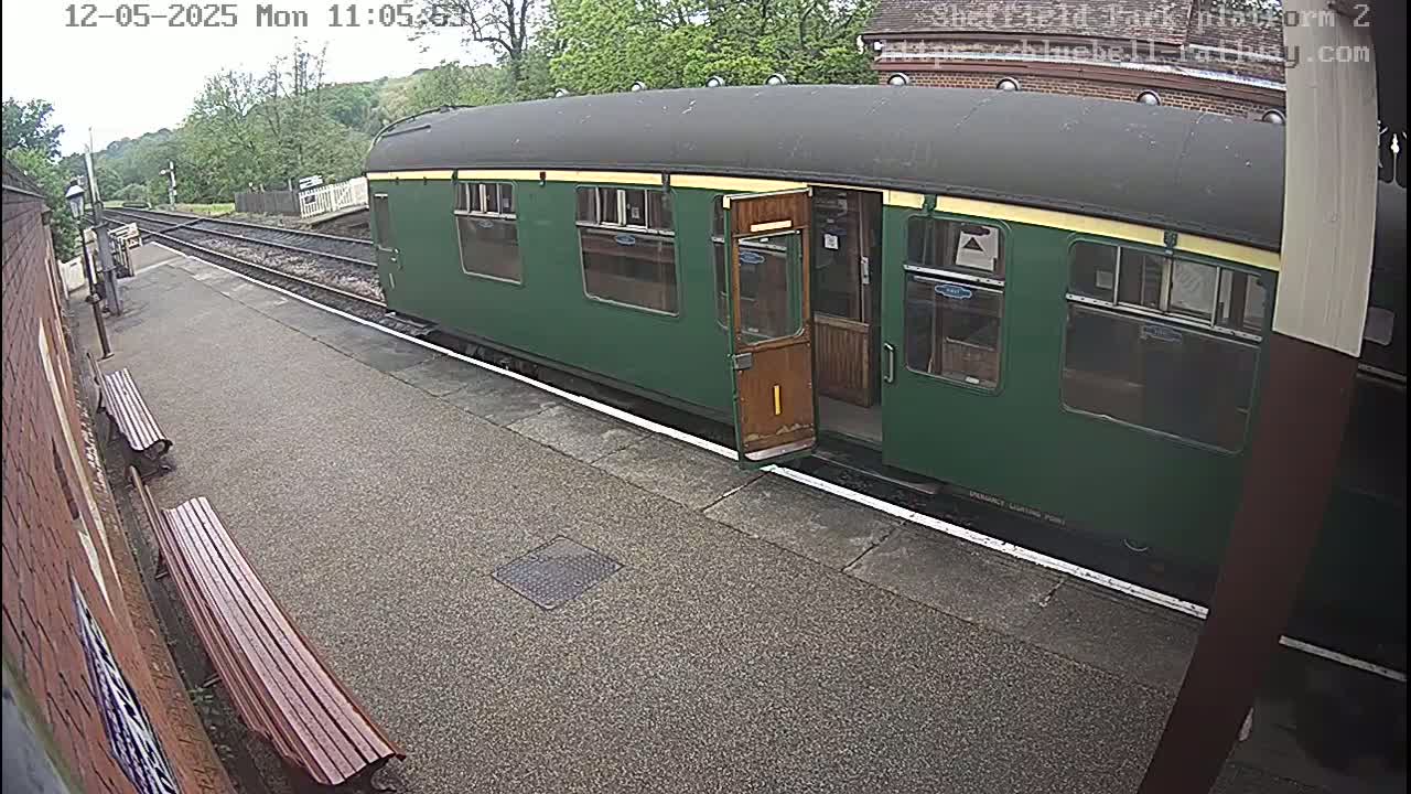 A green passenger train car is stopped at a station platform on an overcast day.
