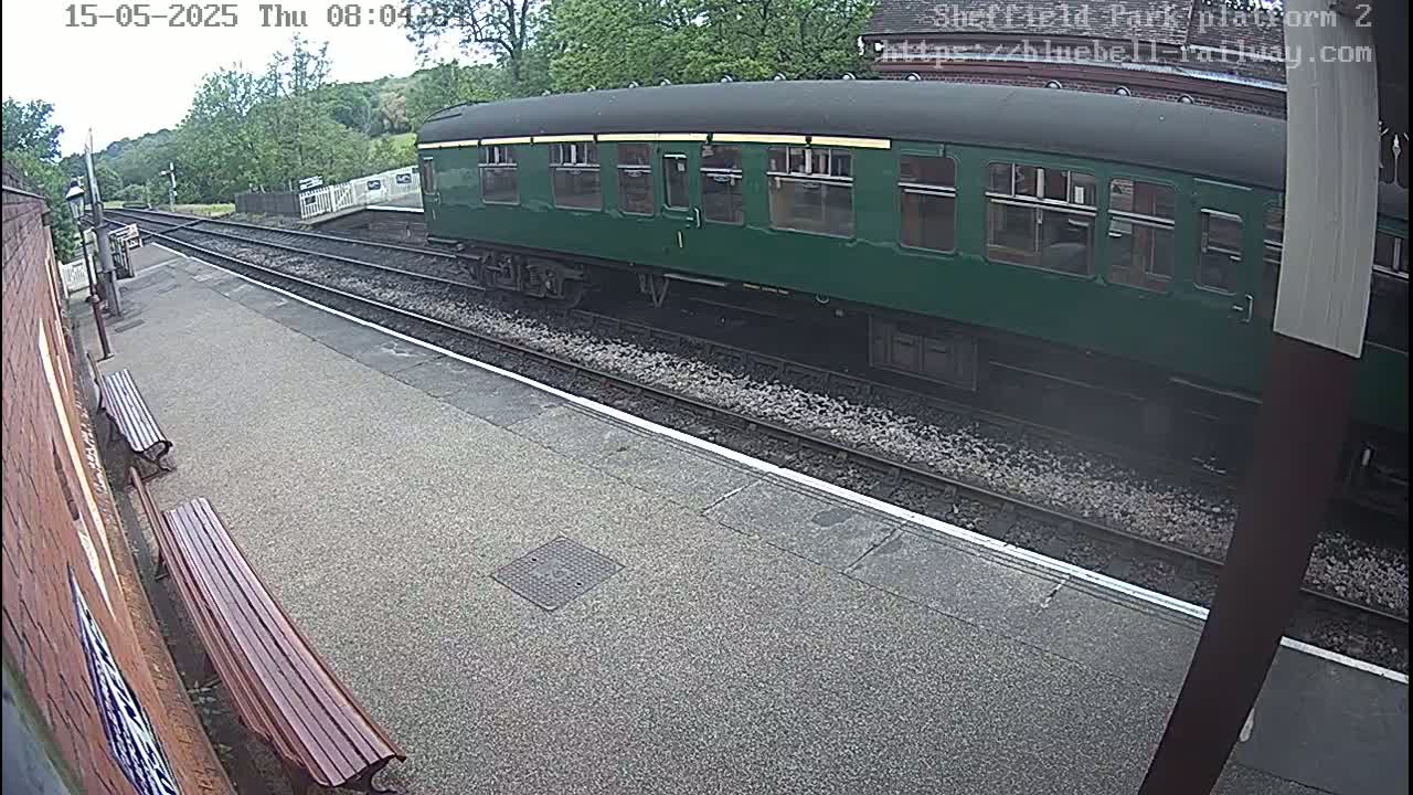 A dark-green railway carriage is parked at a station platform on an overcast day.