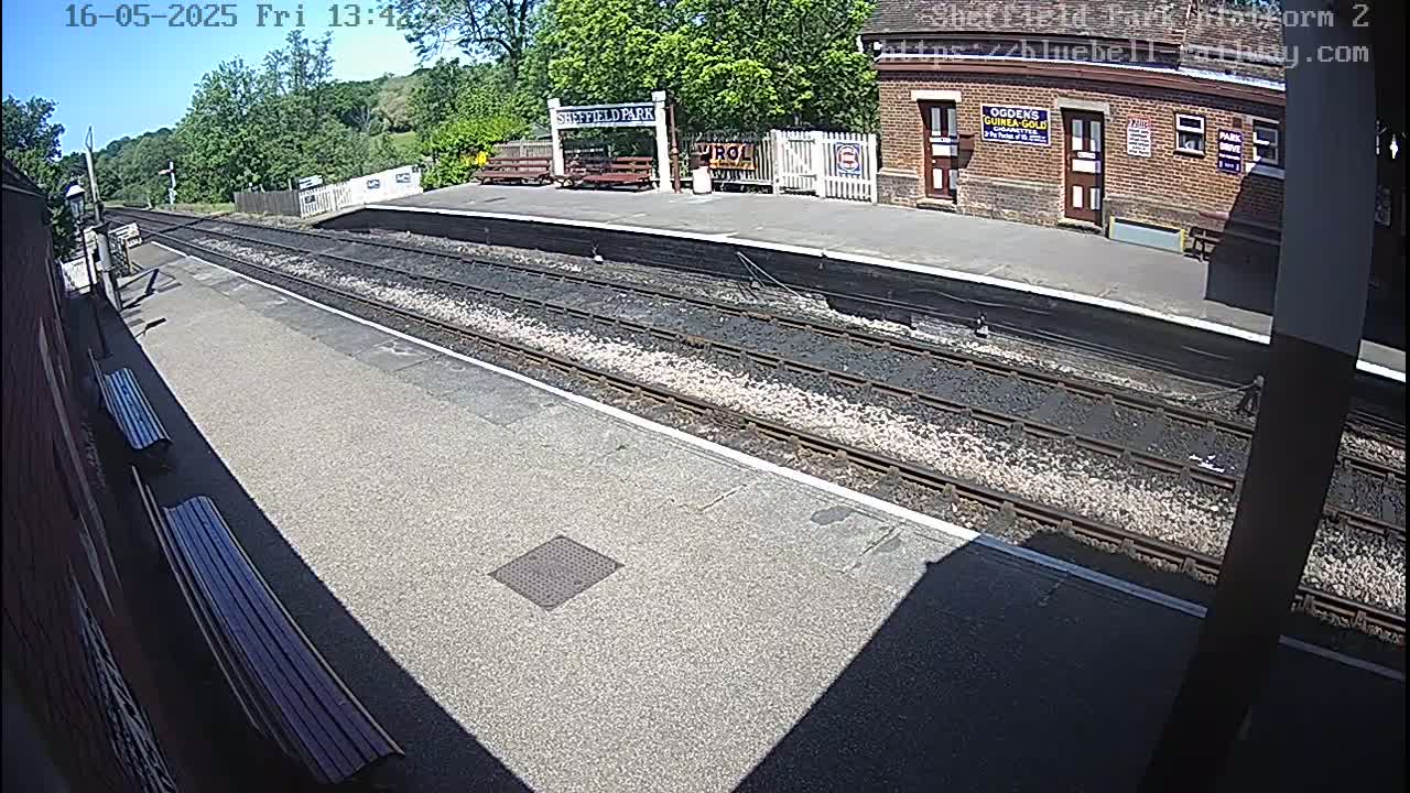 A sunny view of a train station platform with train tracks and benches, under a clear sky.
