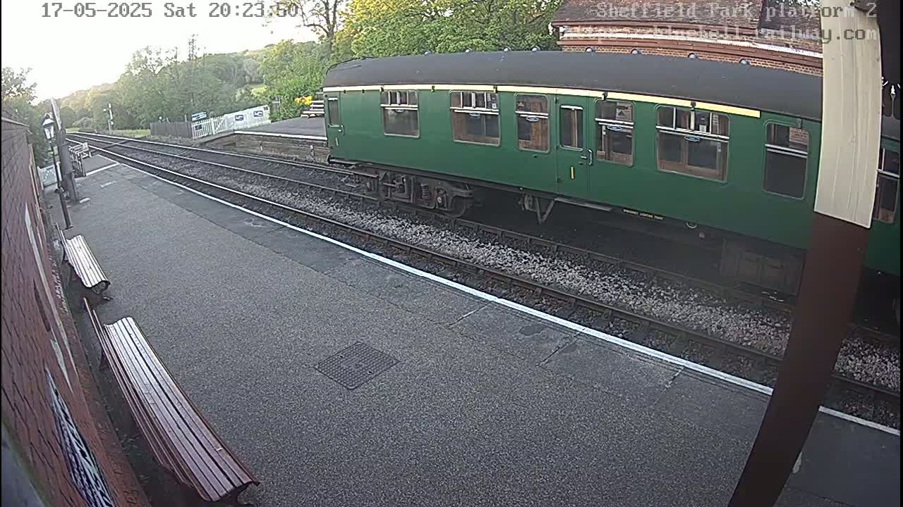 A dark green passenger train car sits on a railway track at a station platform under a twilight sky.