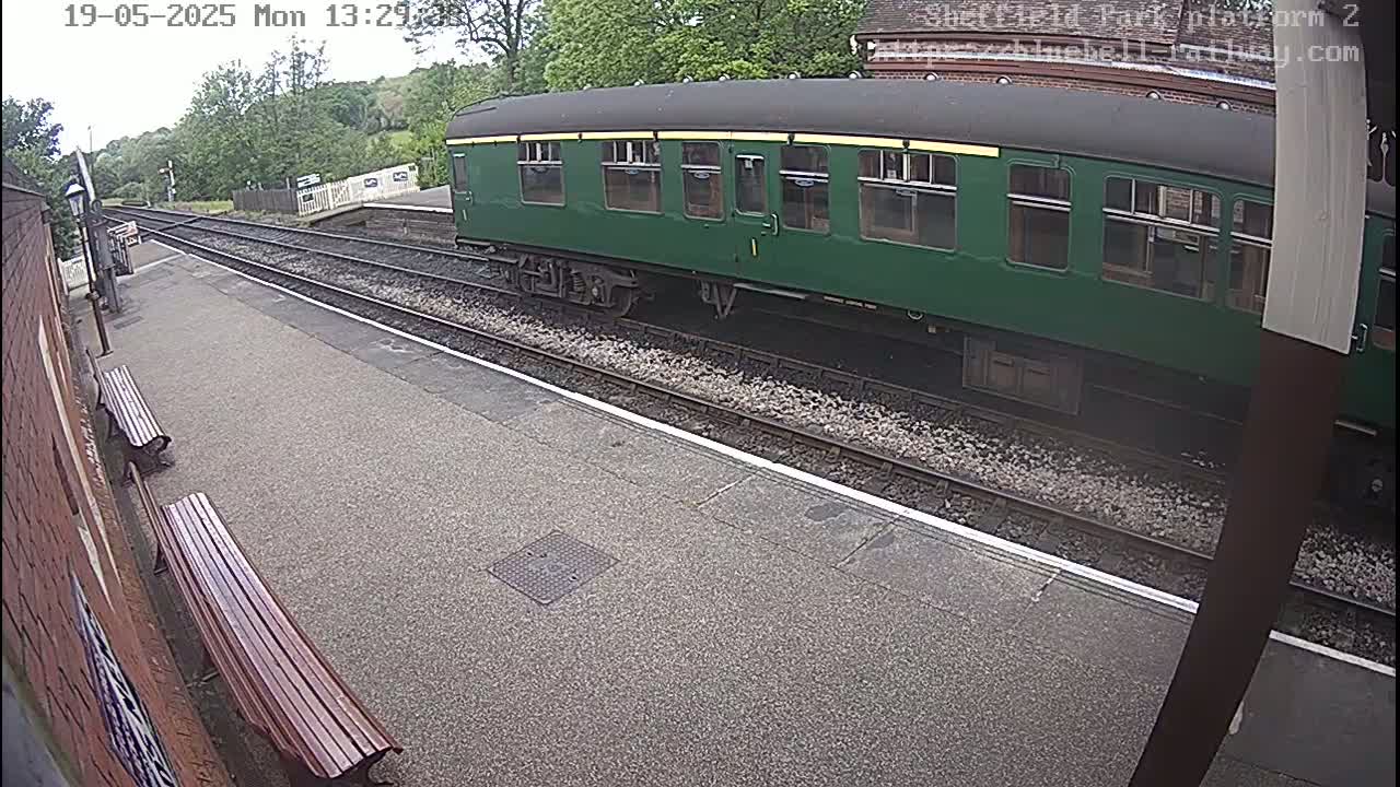 A dark green railway carriage sits at a station platform on an overcast day.