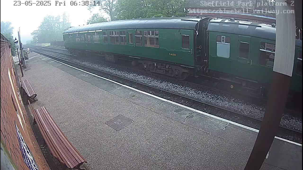 A long, dark-green train car is at a station platform in foggy conditions.