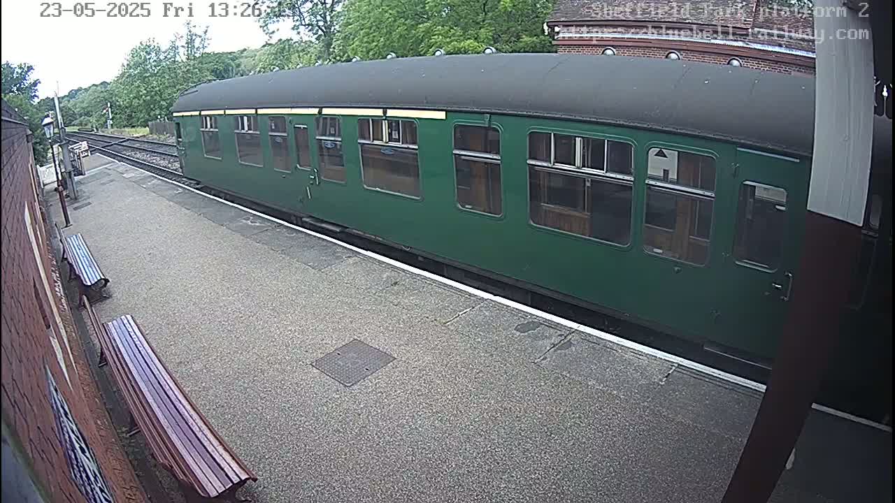 A green passenger train car sits at a station platform on an overcast day.