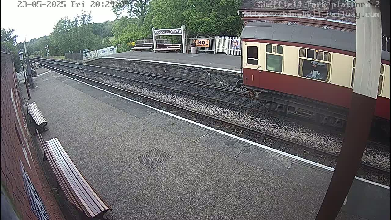 A maroon and cream train is partially visible at a train station platform on an overcast day.