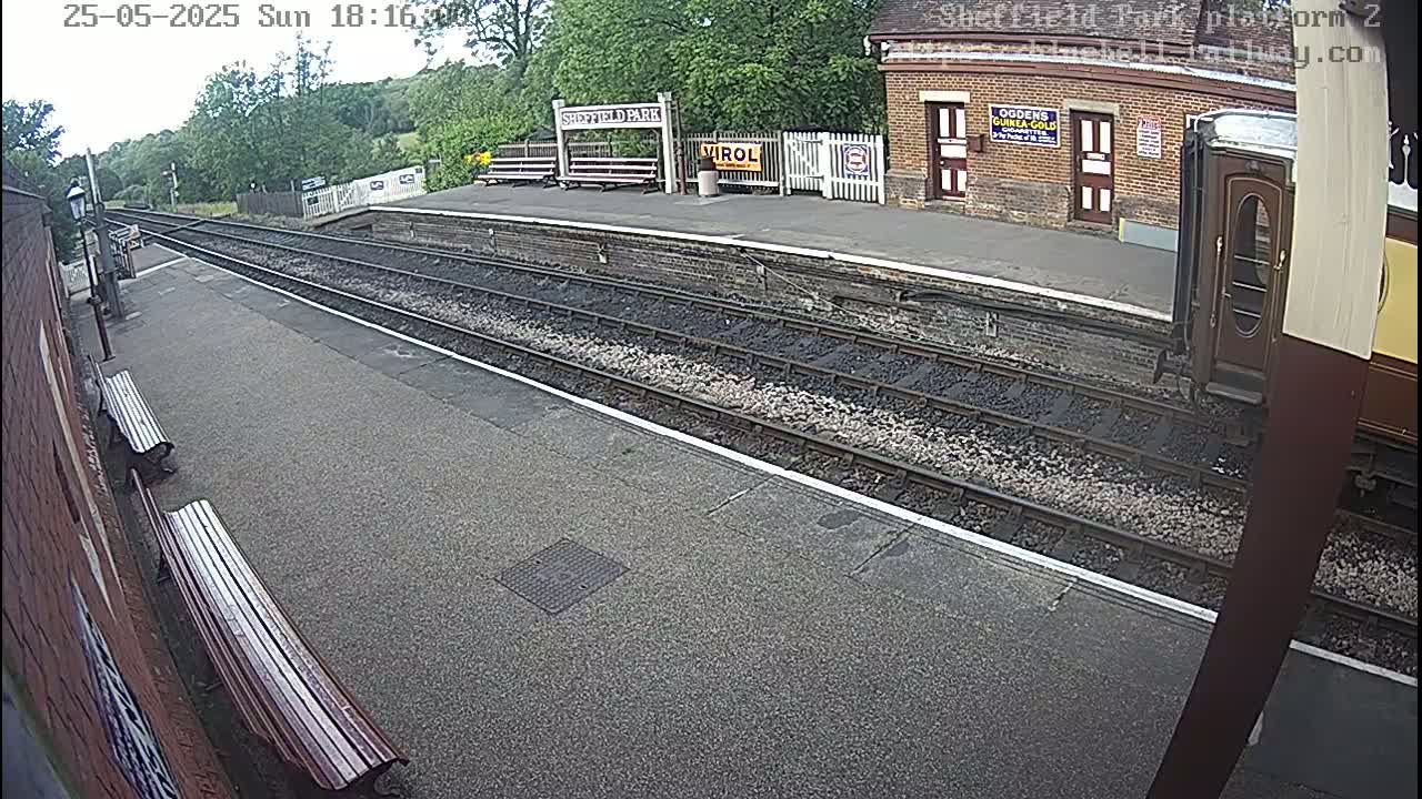A train platform with railway tracks, benches, and a partially visible train car under a partly cloudy sky.