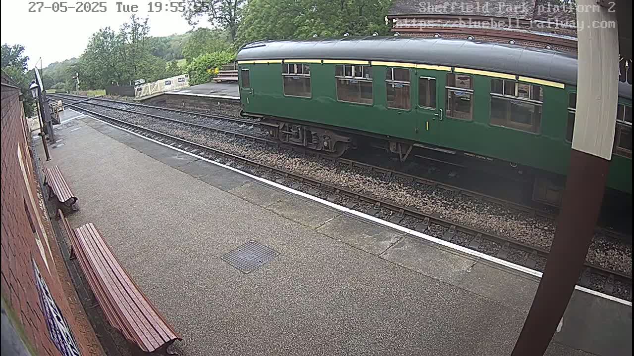 A dark-green passenger railcar sits at a train station platform on an overcast day.