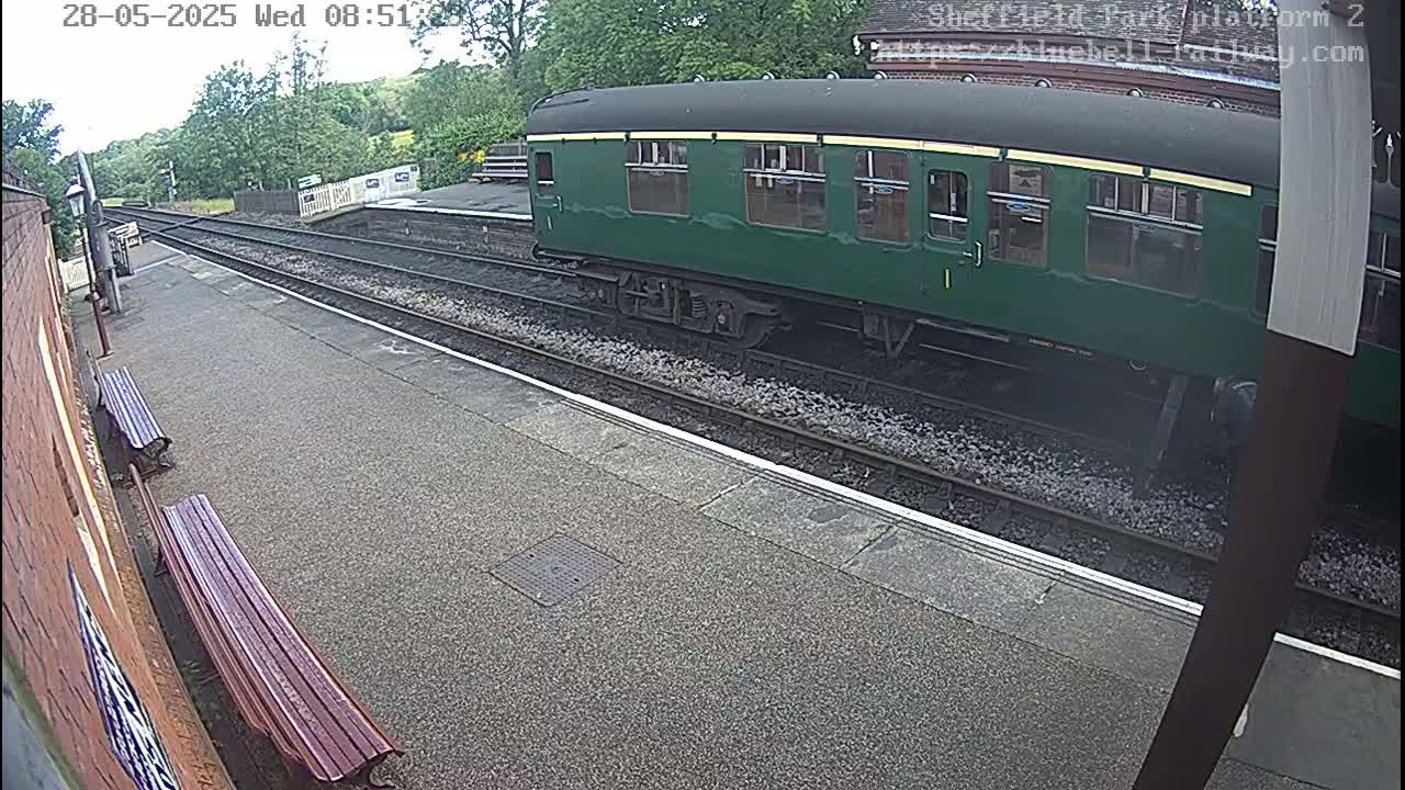 A dark-green railway carriage is parked at a station platform on a partly cloudy day.