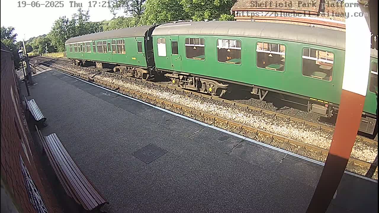 A long green train sits on a railway track on a sunny day.
