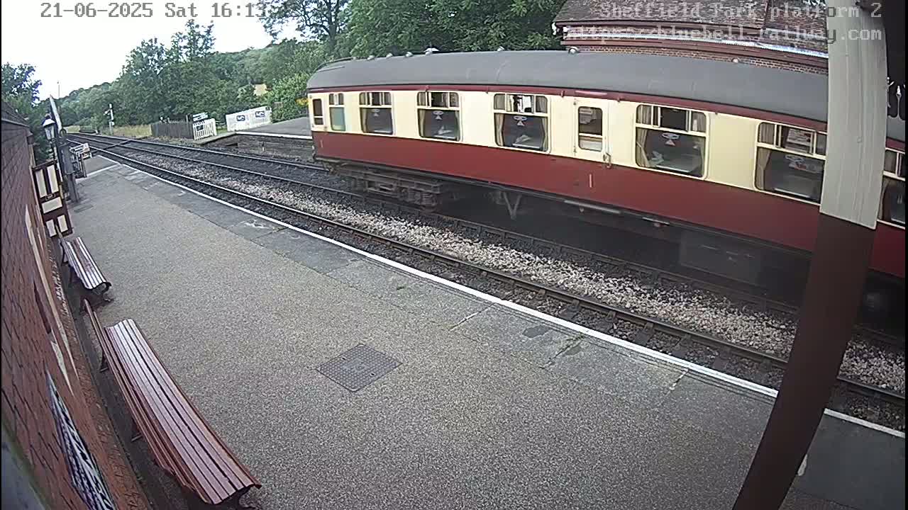 A maroon and cream train is stopped at a railway station platform on an overcast day.