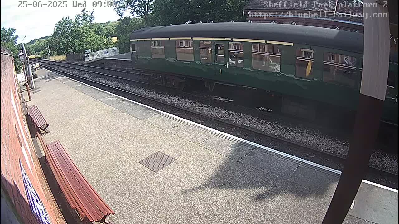 A dark green railway carriage is parked at a station platform on a sunny day.