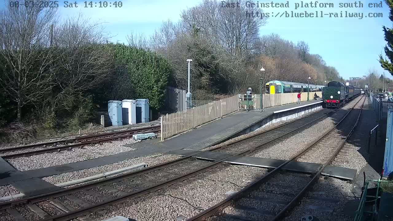 A diesel locomotive and a passenger train are at a train station on a sunny day.