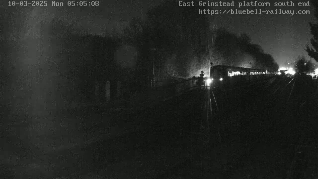 A dimly lit nighttime scene shows a train emitting smoke as it sits at a platform.
