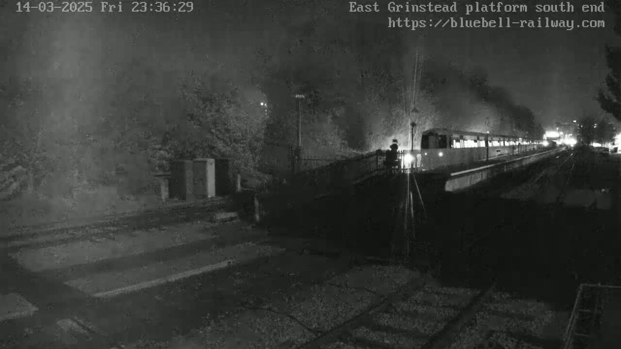 A train is at a nighttime station platform, partially obscured by darkness and possibly fog or smoke.