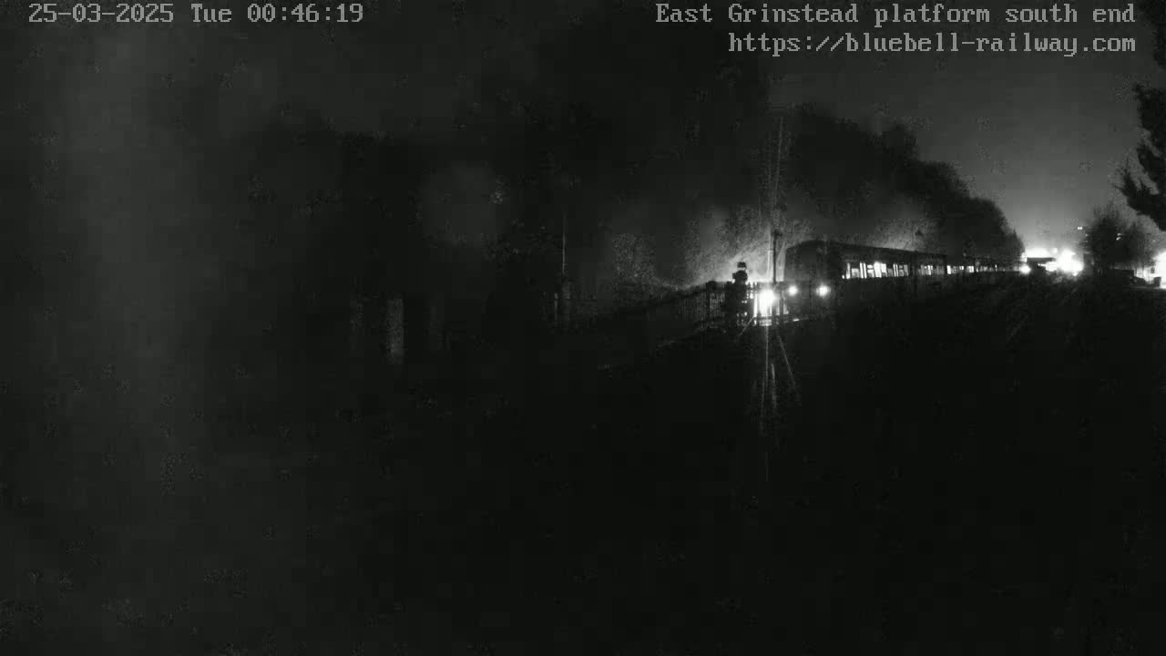 A dimly lit train is partially visible at night, emitting smoke from its engine.