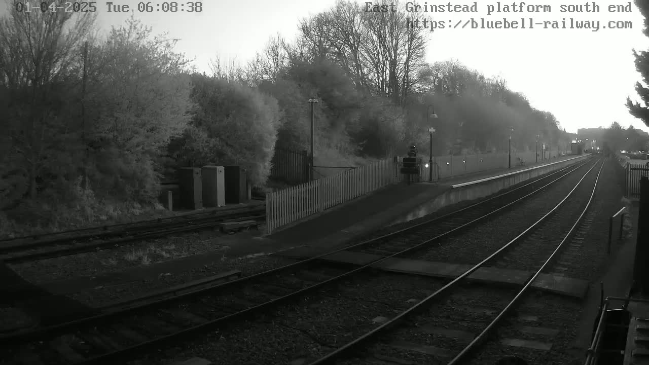 A dimly lit train station platform with two sets of train tracks extending into the distance under a hazy sky.