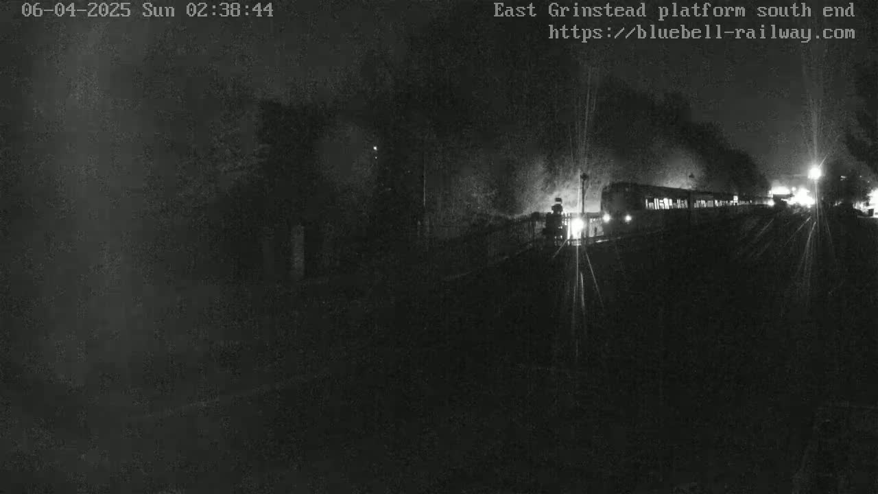 A dimly lit nighttime view shows a train departing from a station platform.