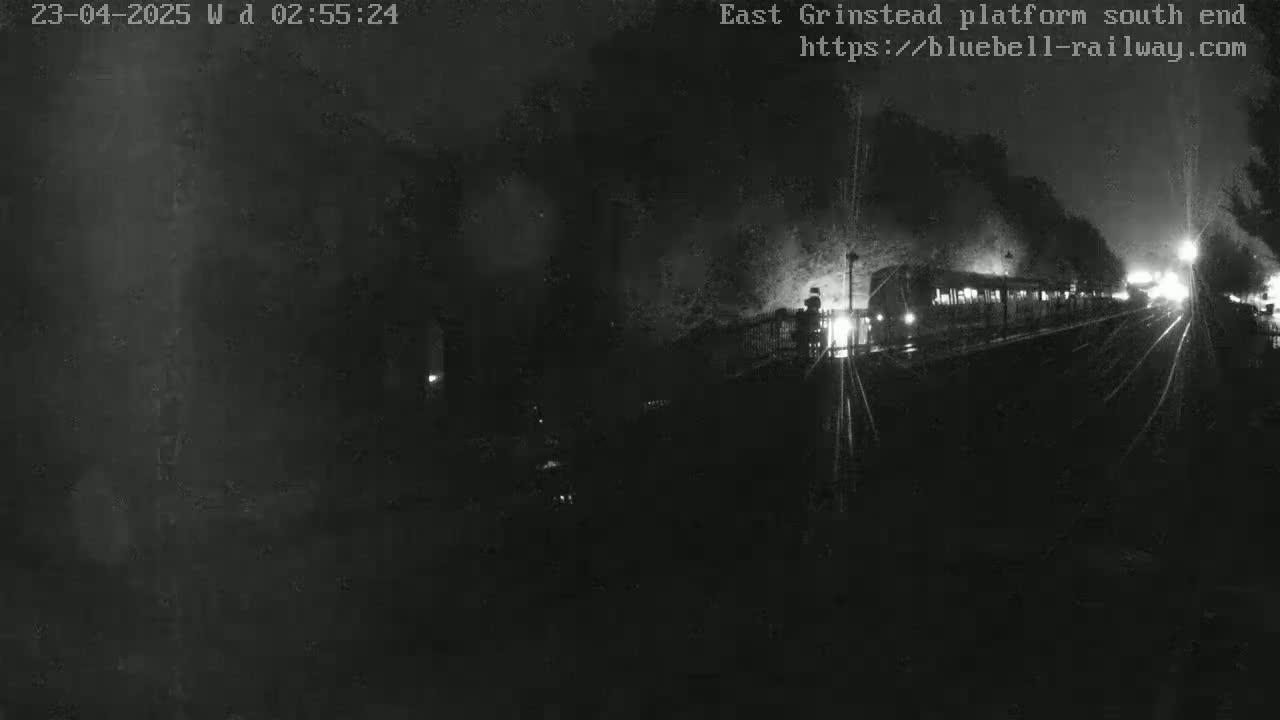 A dimly lit train departs a platform at night, emitting smoke and light.