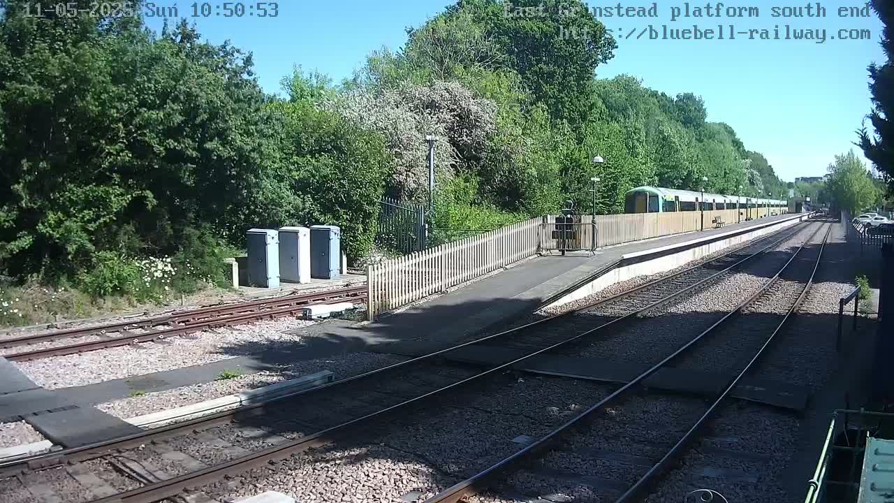 A train is stopped at a platform next to a wooded area on a sunny day.