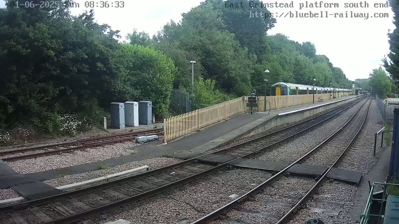 A train sits at a station platform next to a wood fence on an overcast day.