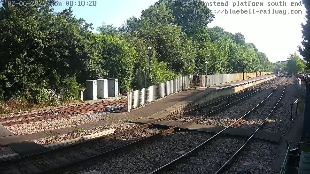 A sunny view of a train platform with several tracks extending into a lush green landscape.
