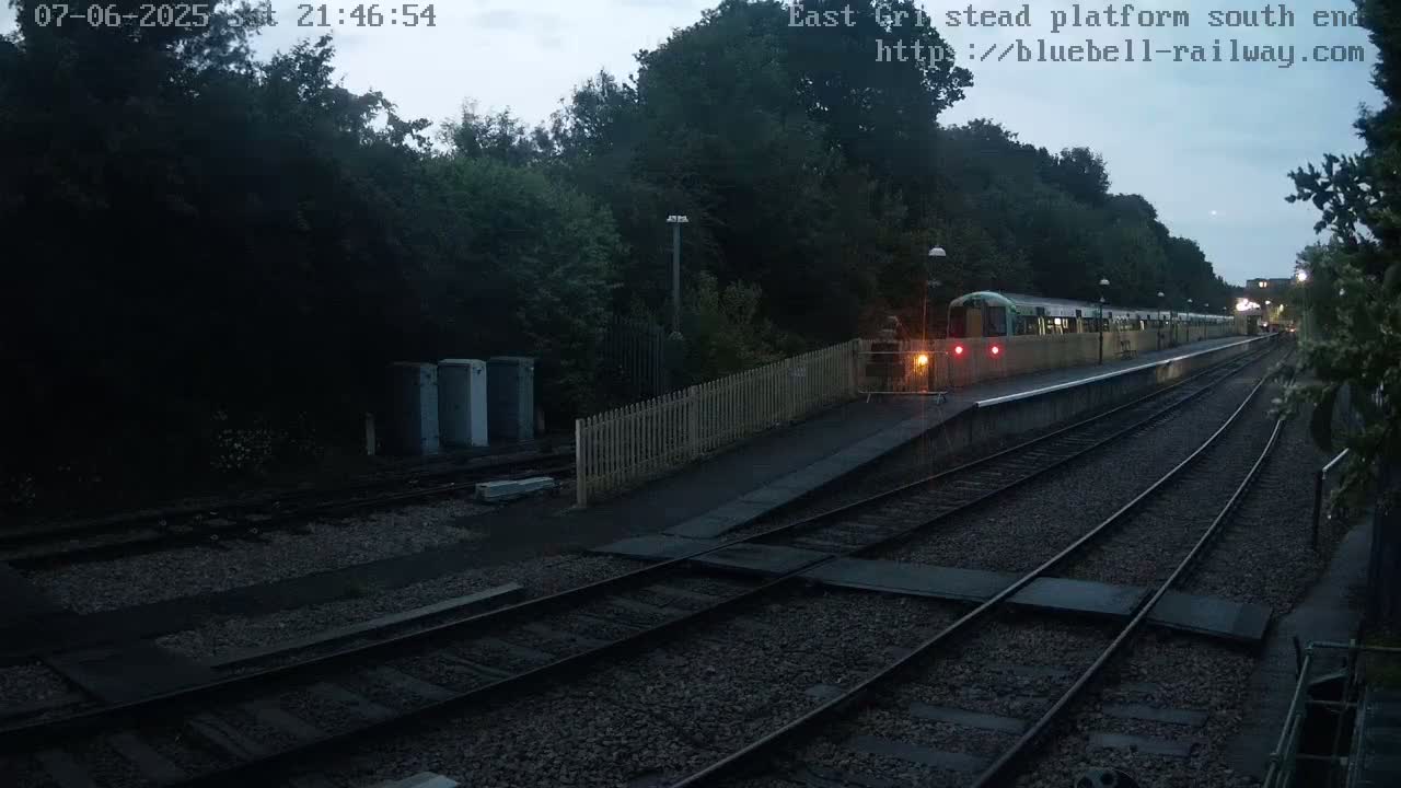 A train is stopped at a dimly lit station platform under a twilight sky.