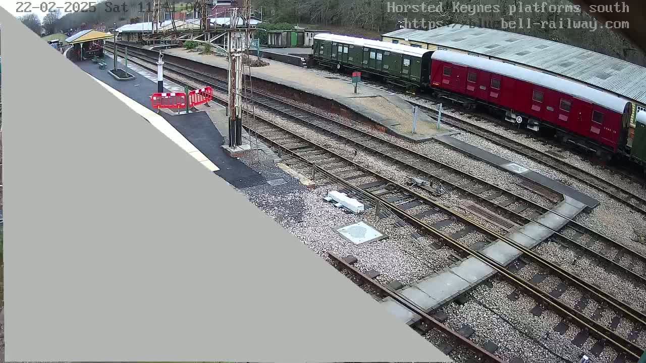 A high-angle view of a train station with multiple train tracks, a platform, and two passenger cars, one green and one red, under an overcast sky.