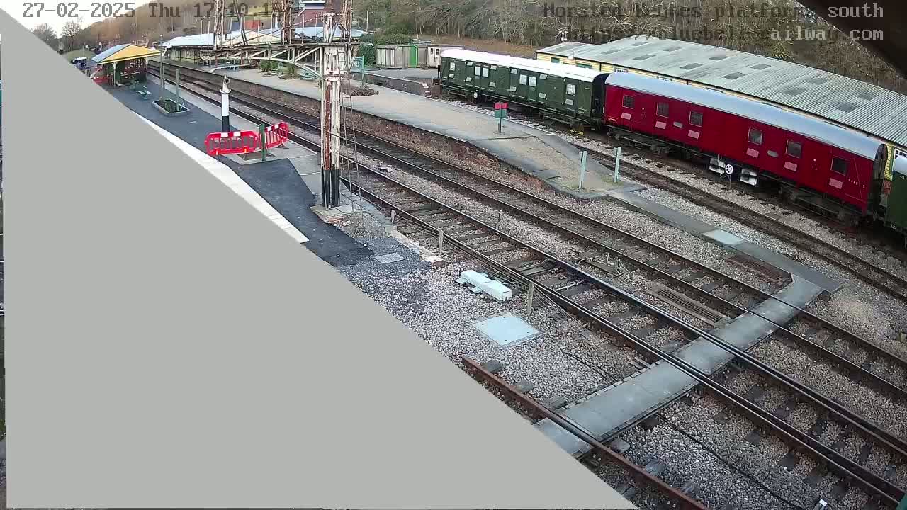 A high-angle view shows a railway station with several train cars, some green and one red, parked on the tracks on an overcast day.